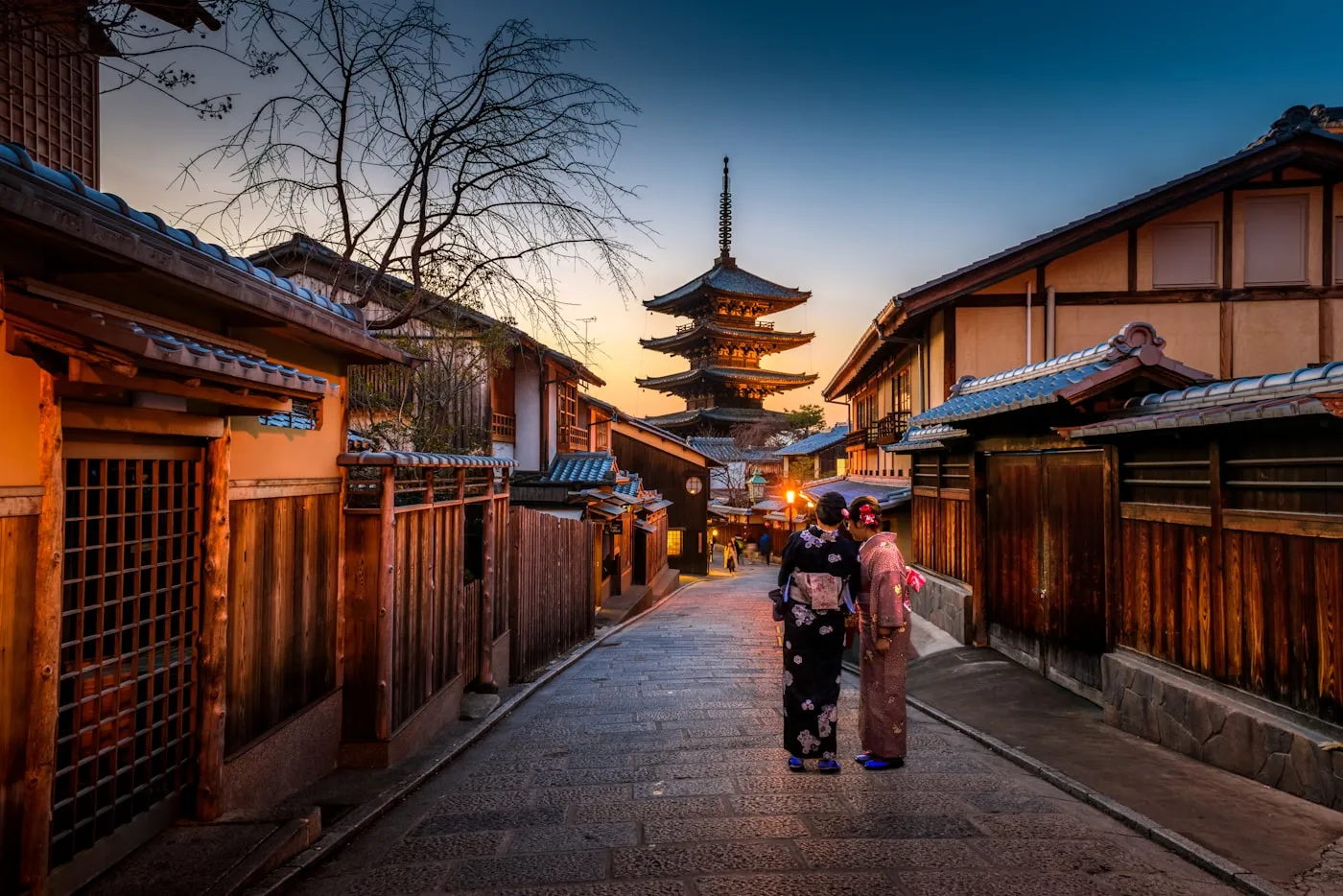 Two people in kimono walking a lantern-lit lane toward Yasaka Pagoda, Kyoto